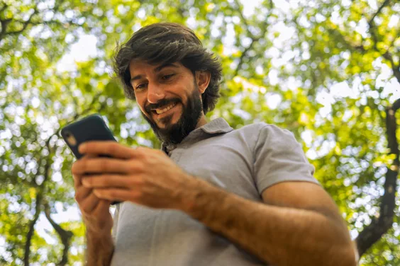 Pessoa sorrindo ao olhar o celular ao ar livre