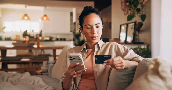 Pessoa segurando o celular e um cartão de crédito em casa