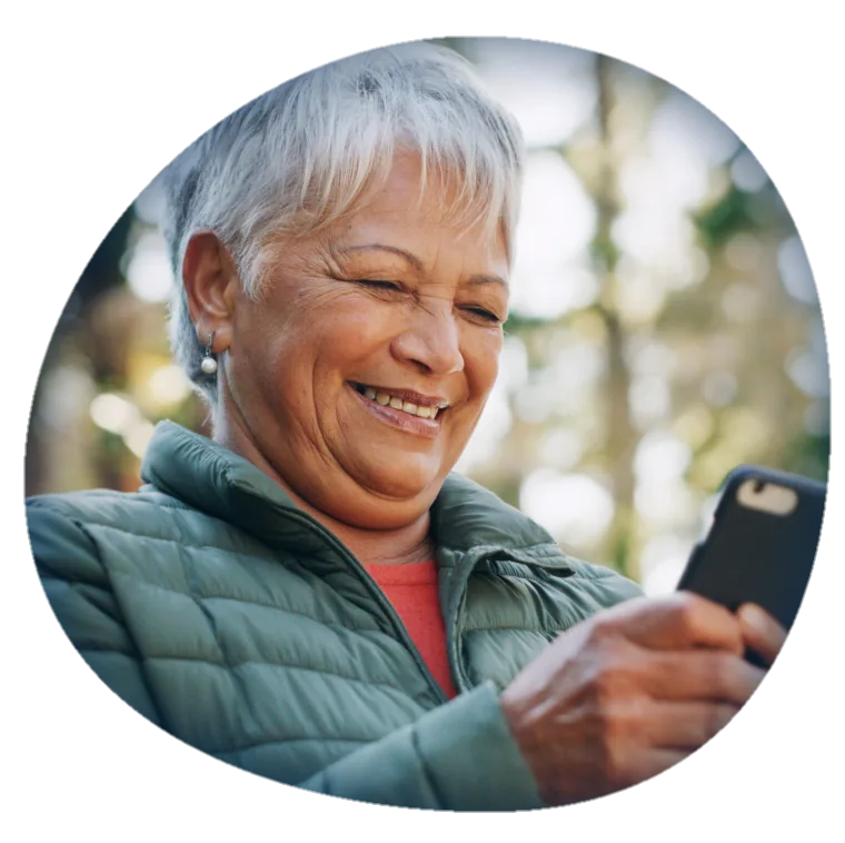 Mulher sorrindo enquanto usa o celular ao ar livre