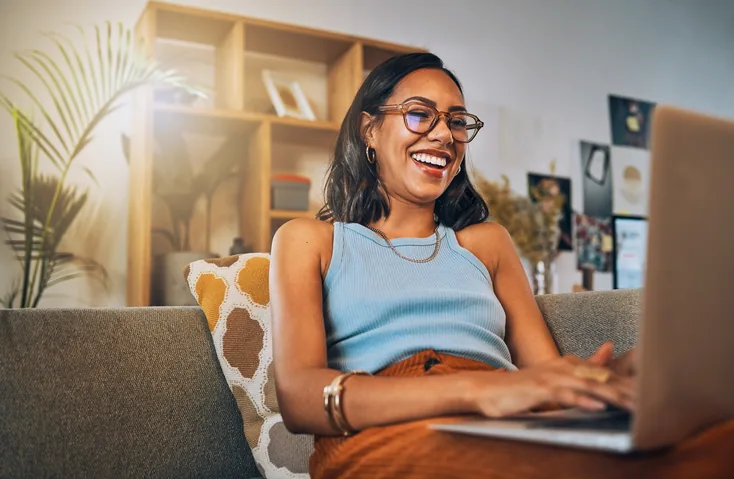 Mulher sorrindo no sofá enquanto usa o notebook