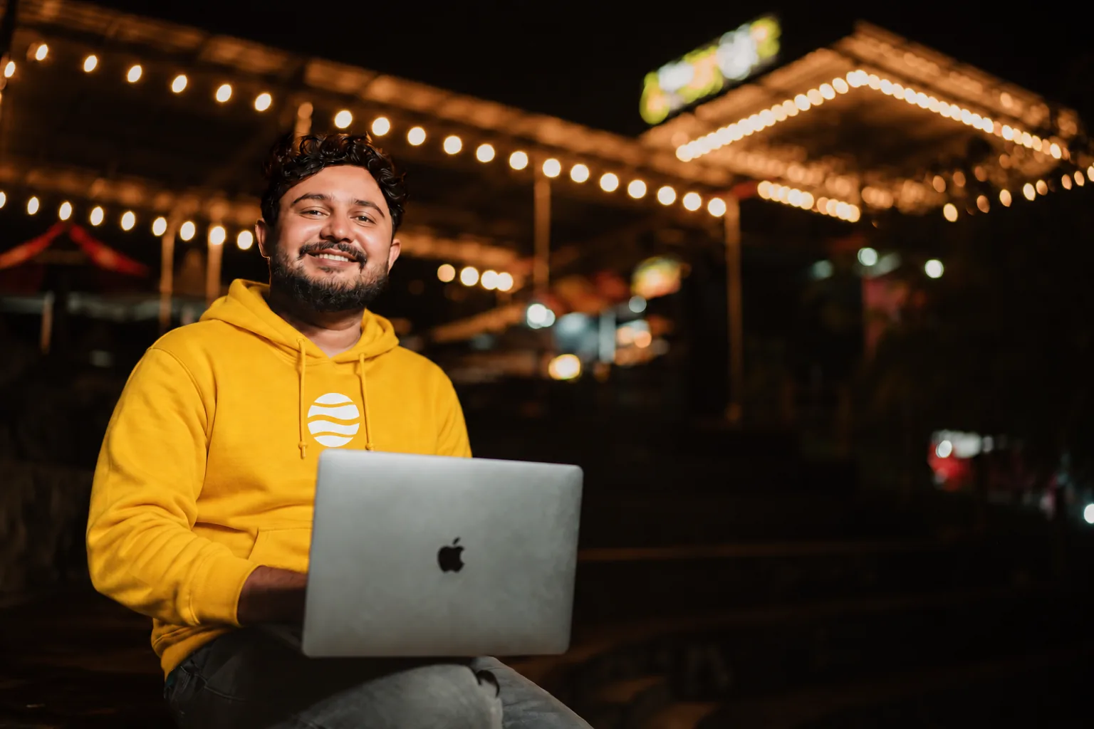 Produtor sorrindo com um notebook no colo, vestindo moletom amarelo da Eduzz