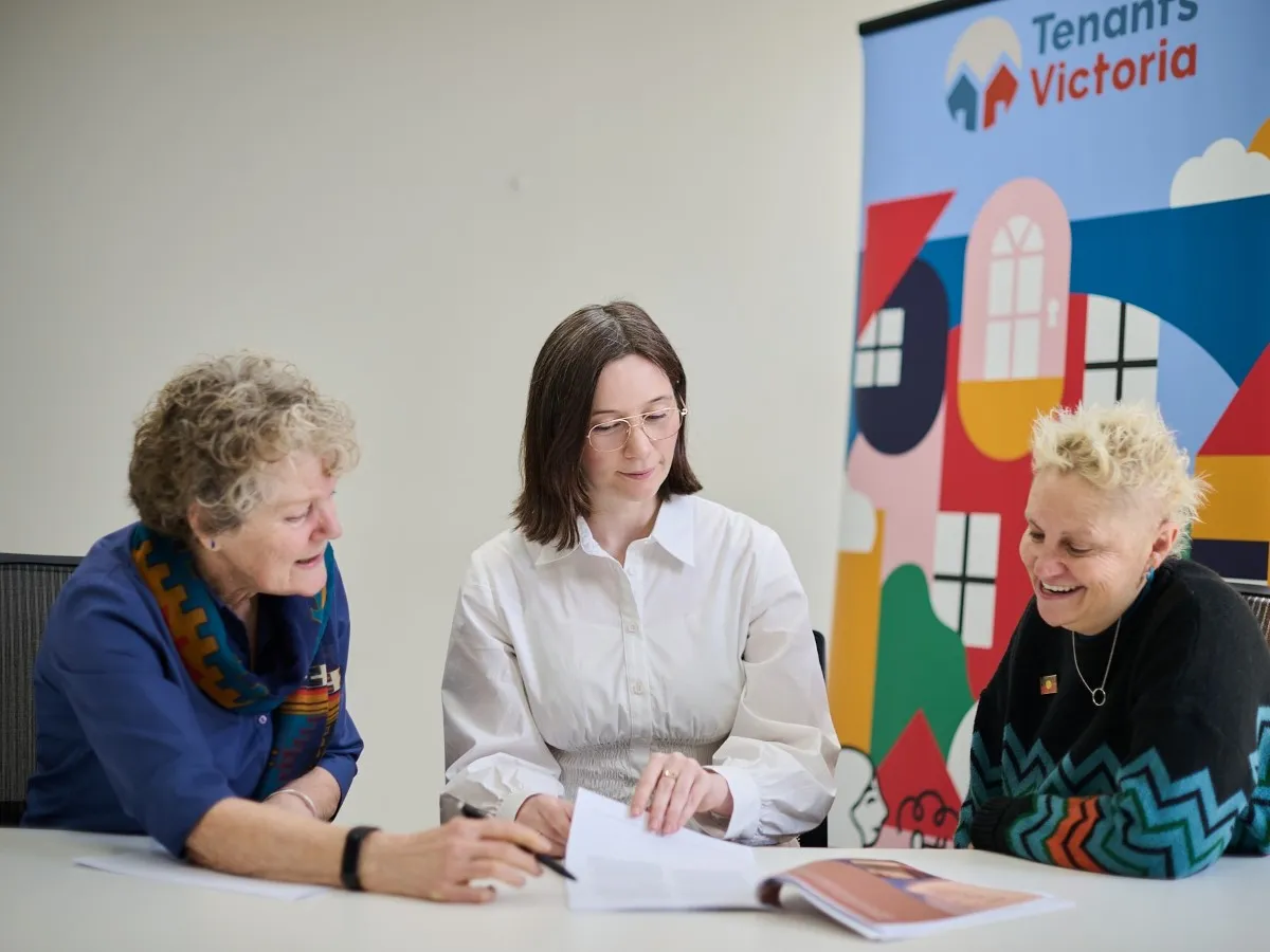 Three people seated at a table discussing documents, with a colourful abstract banner in the background.