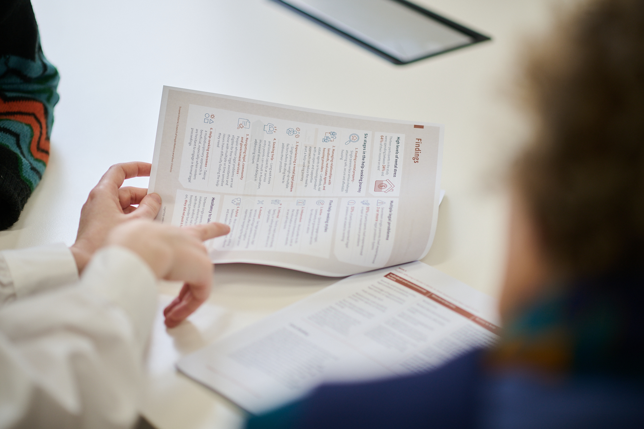 Two people seated at a table reviewing a multi-section document with small icons; another document is partially visible