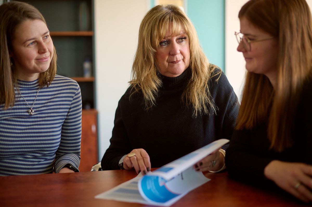 Three people sitting around a table looking at a document.