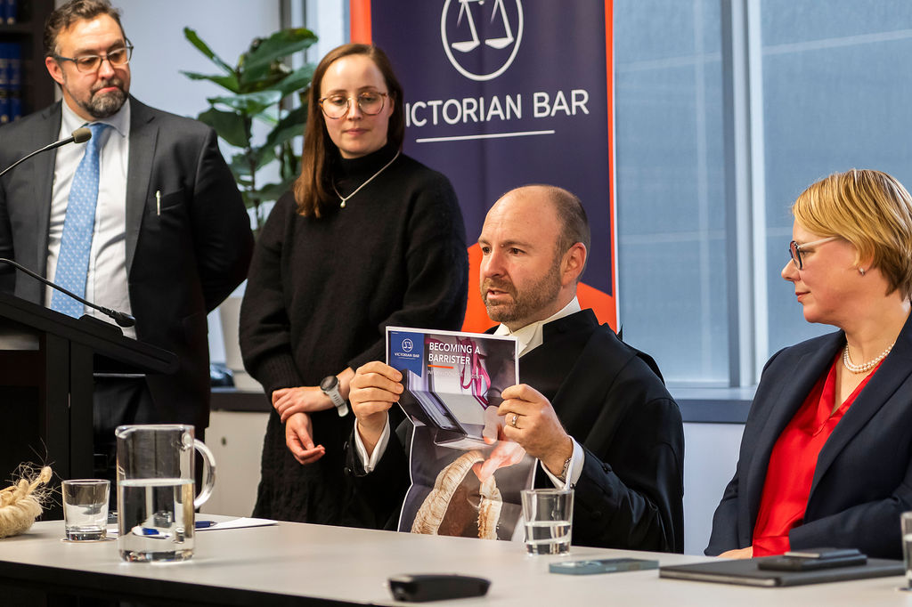 Panel at table with microphone and water glasses; one person holds a booklet titled “Becoming a Barrister,” with “Victorian Bar” banner behind.