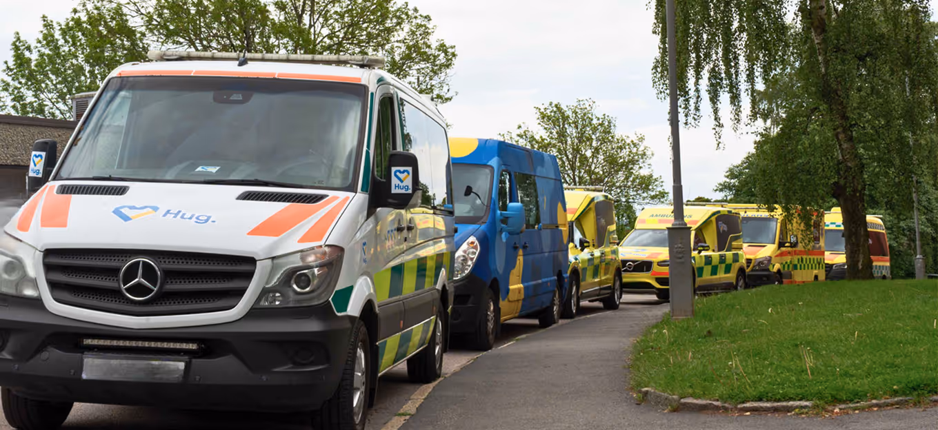 Line of parked emergency and rescue vehicles including white and yellow ambulances on a tree-lined street.