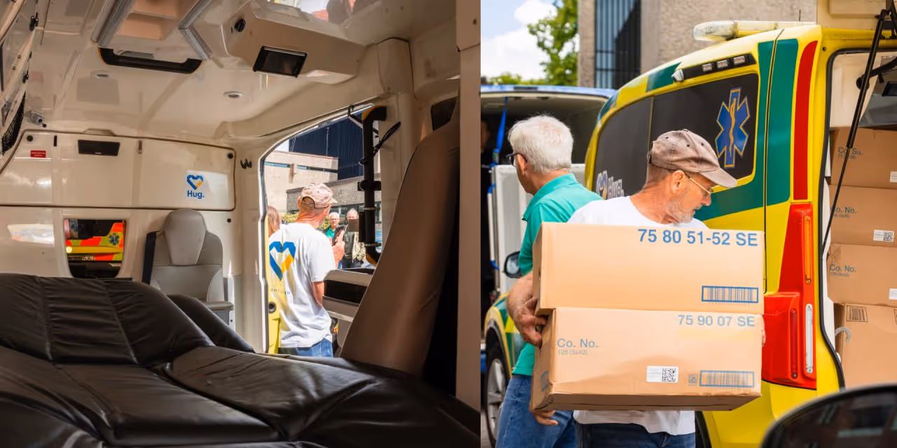 Man wearing a cap carrying two stacked cardboard boxes beside a yellow and green ambulance with open rear doors.