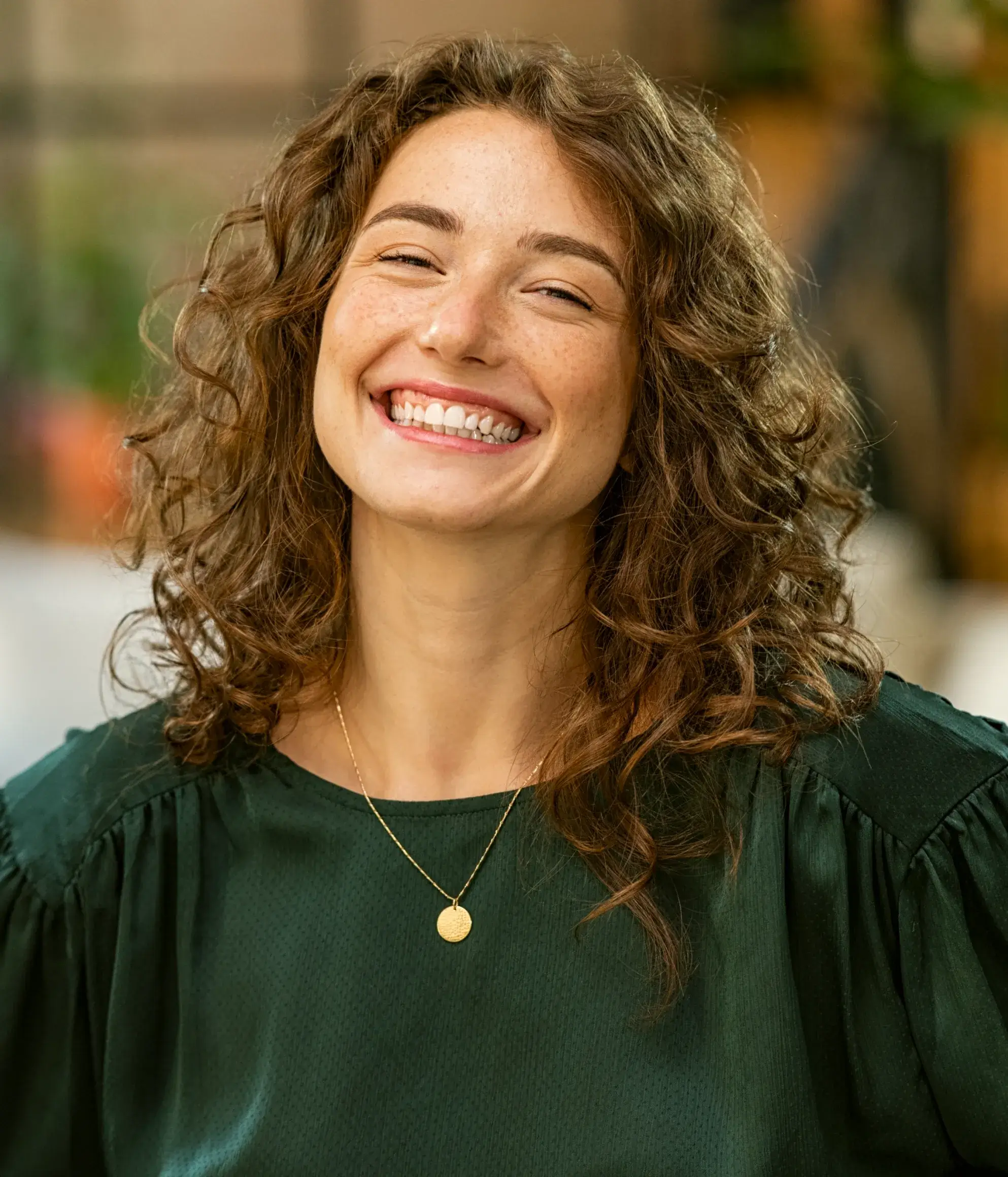 a woman with curly hair smiling and wearing a green top