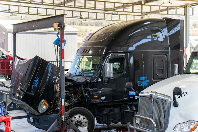 DOT inspection on a heavy-duty semi-truck in a service bay with hood raised, allowing technicians to inspect engine, safety, and compliance systems.