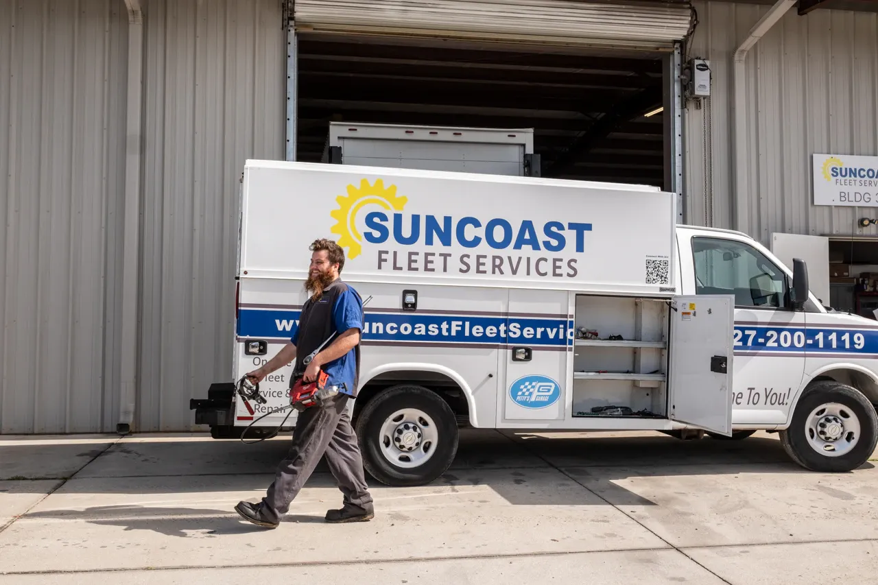 Mobile heavy-duty service truck parked outside a repair shop with a technician carrying tools. SUNCOAST FLEET SERVICES.