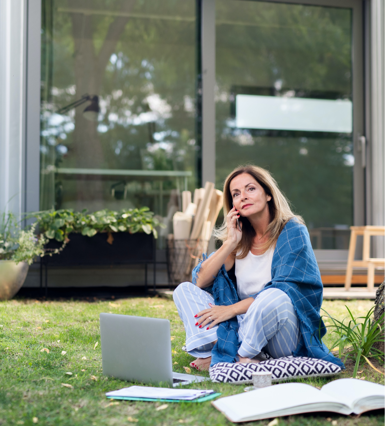 A lady sitting on the floor with her pc outdoors making a call.