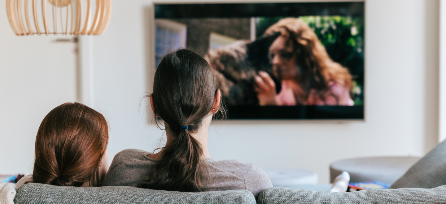 Two ladies sitting on the couch while watching the Tv