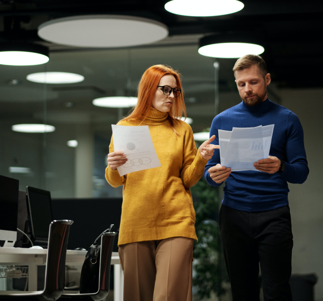 a lady and a man holding papers while discussing.