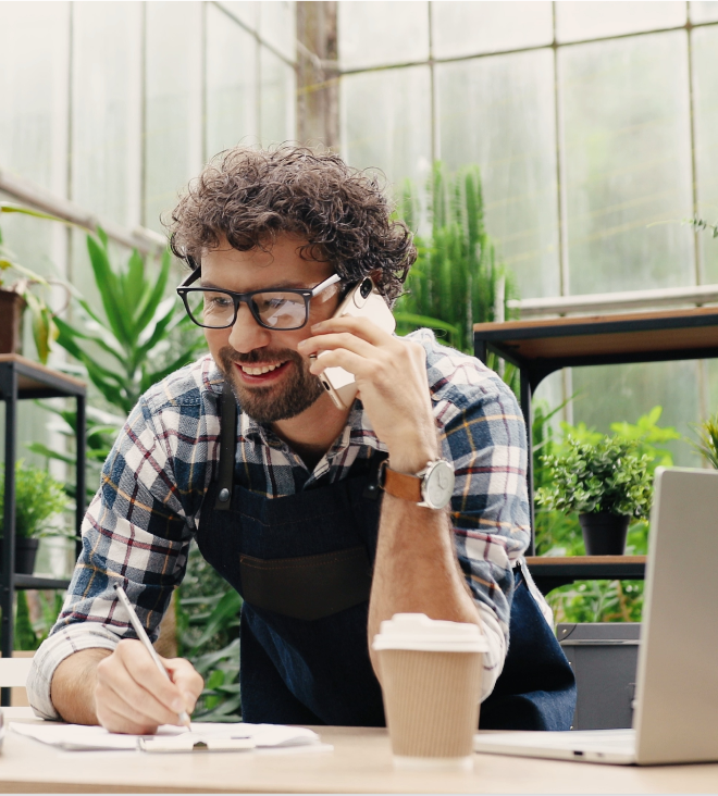 An happy man on a phone call smiling while writing.