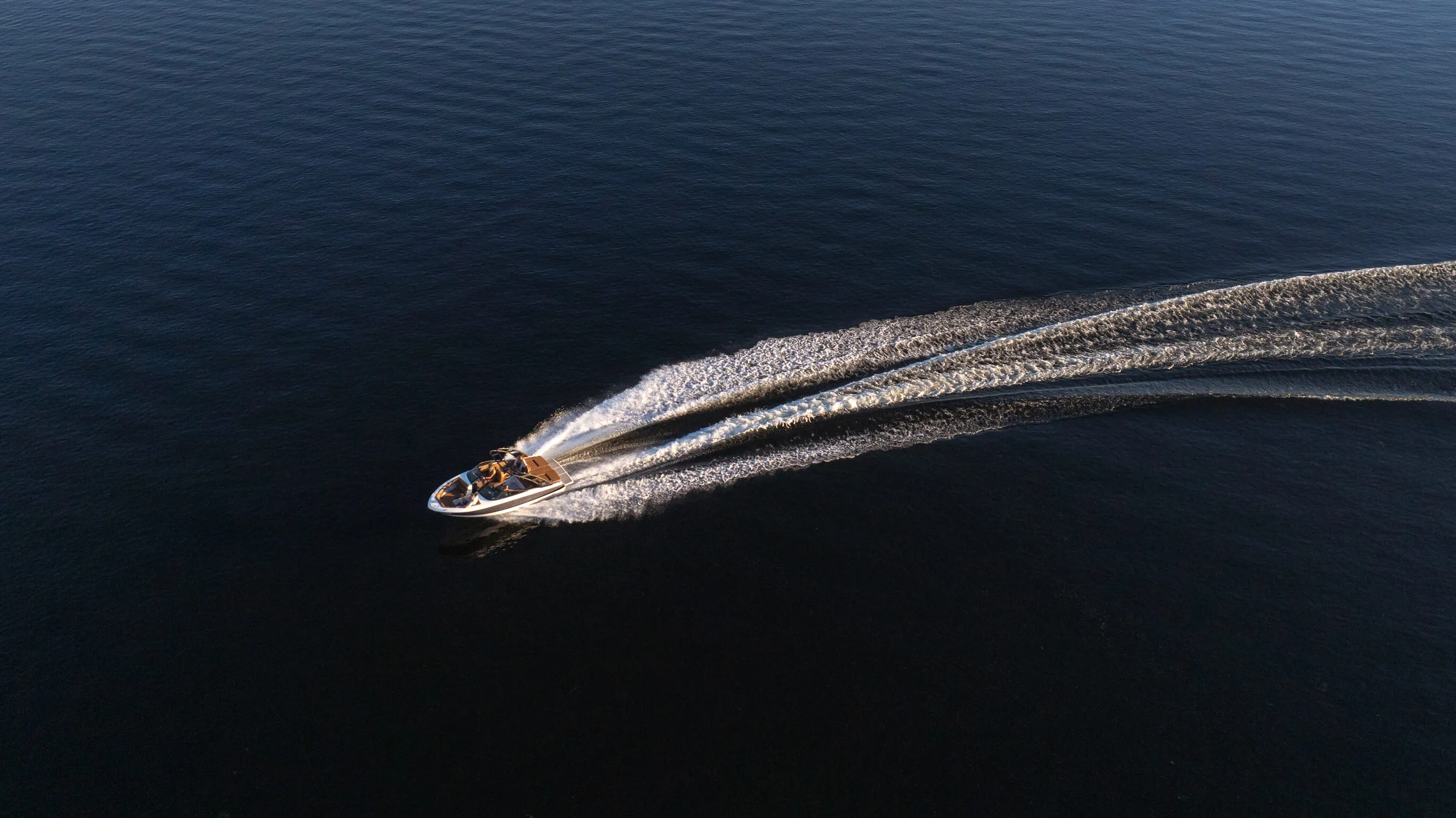 Speedboat making a sharp curved wake on dark blue water.