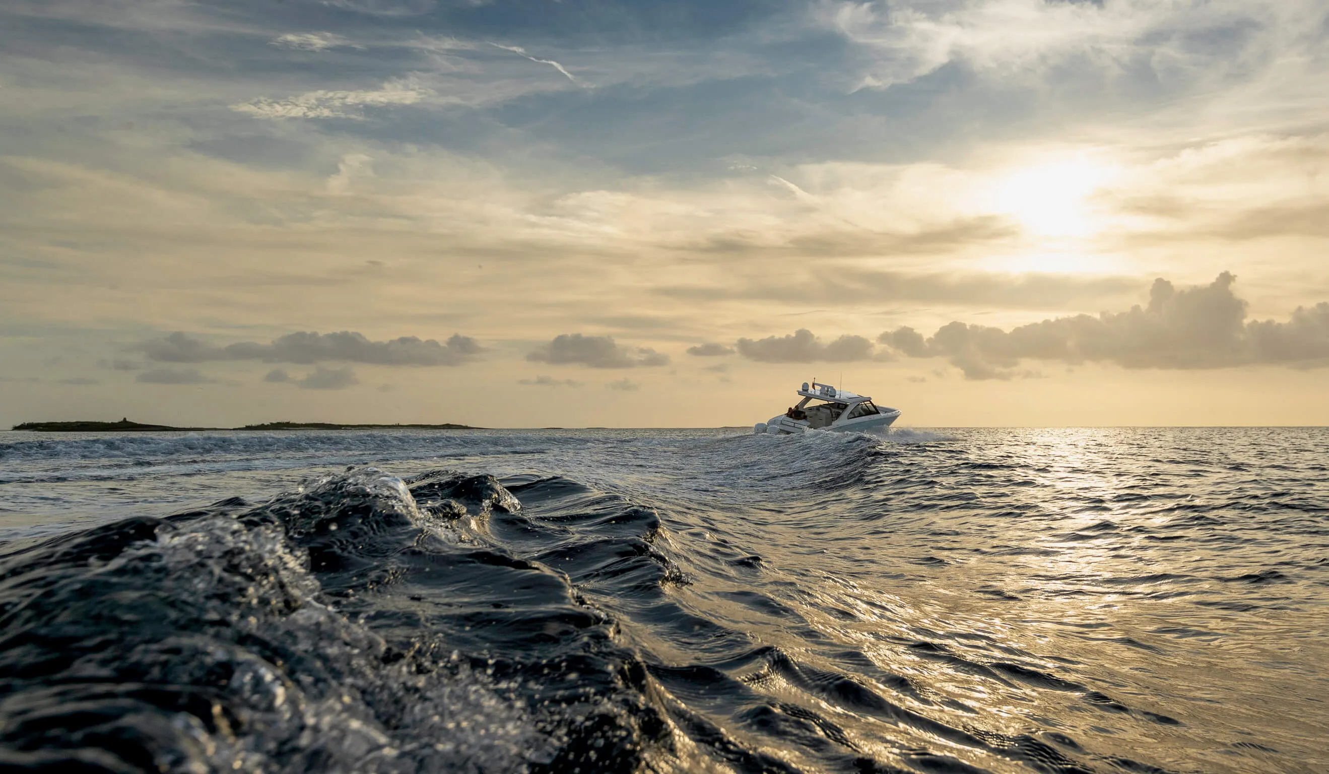 White motorboat creating waves on the ocean at sunset with a partly cloudy sky.
