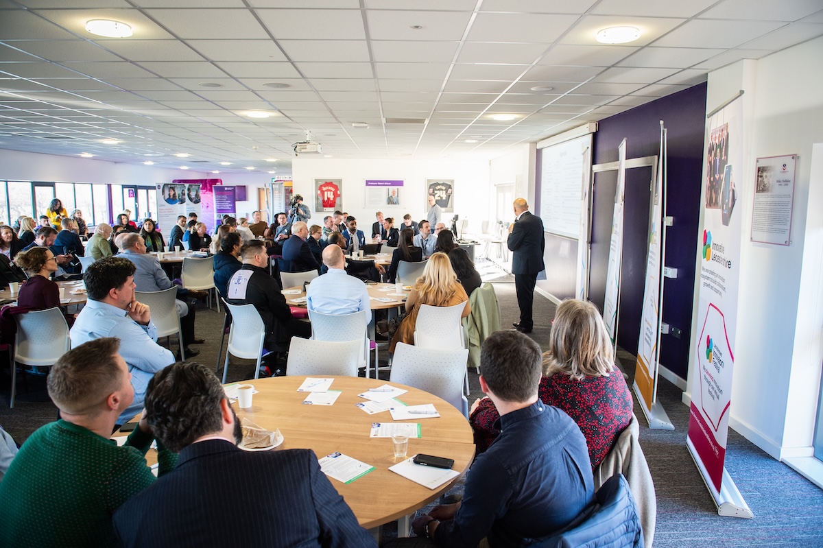 A group of people sat at tables listening to a guest speaker