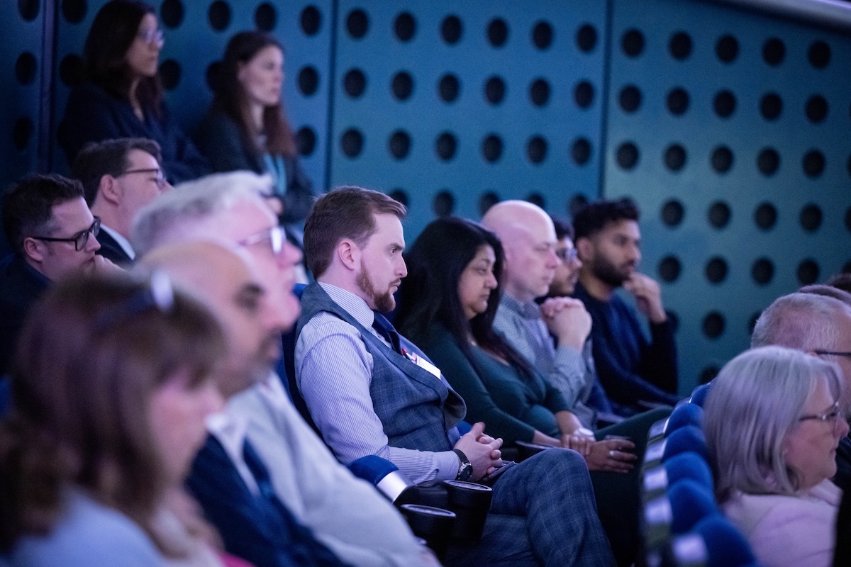 An image showing people sat down in a room listening to a speaker