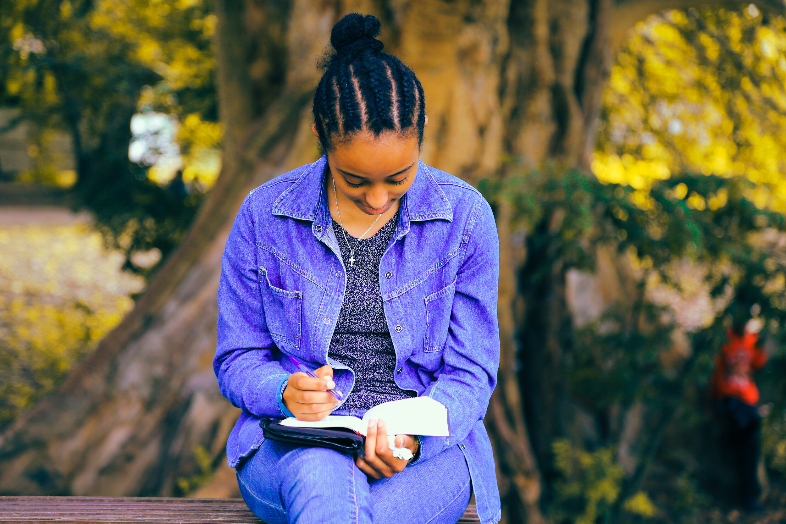 A young woman under a tree looking at a planner