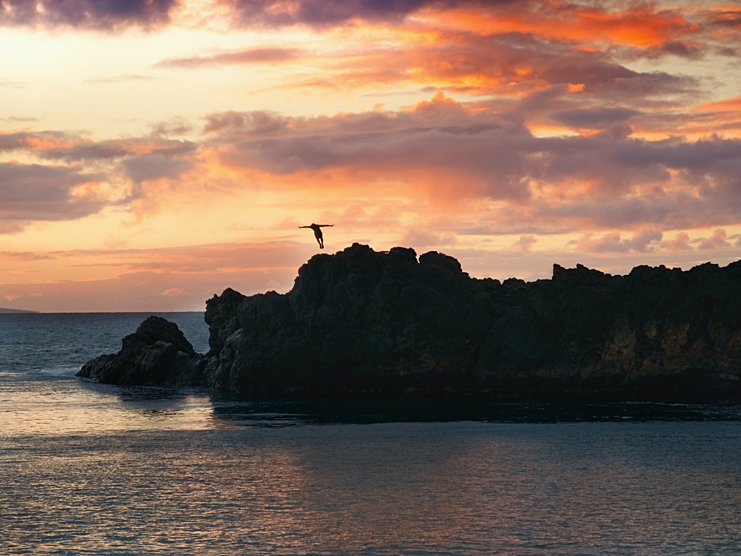 An image of a man diving into the water off a rock