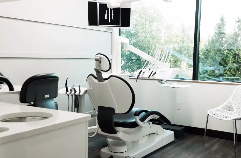 Modern dental office with a dental chair, equipment, and large window showing greenery outside.
