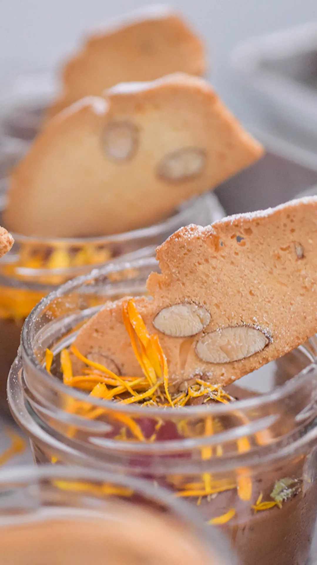 Jars of chocolate pudding topped with biscotti and flower petals.