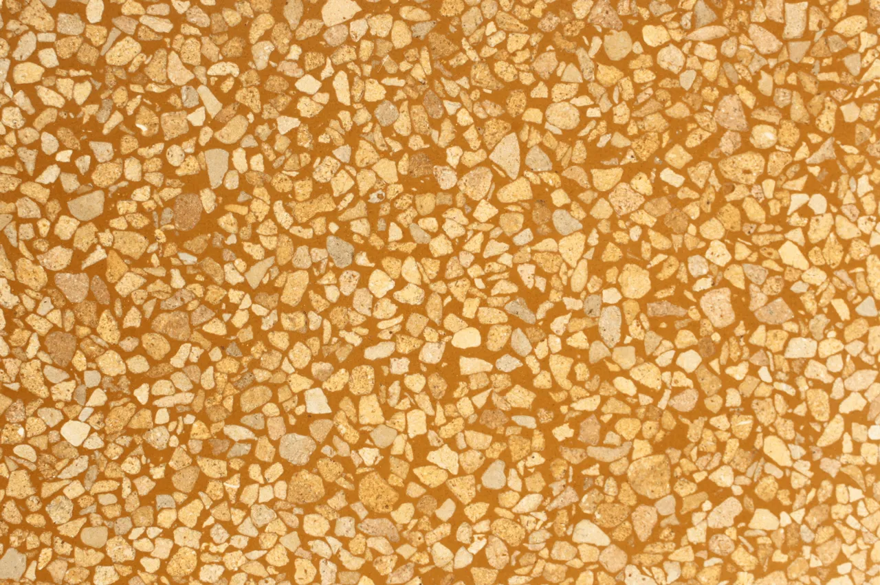 marmorite com base cor-de-laranja e inertes reciclados em pedra portuguesa na cor amarelo / Orange base terrazzo sample with recycled portuguese yellow stone.
