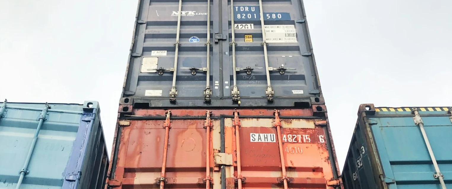 Low-angle view of stacked industrial shipping containers used for international vehicle transport.
