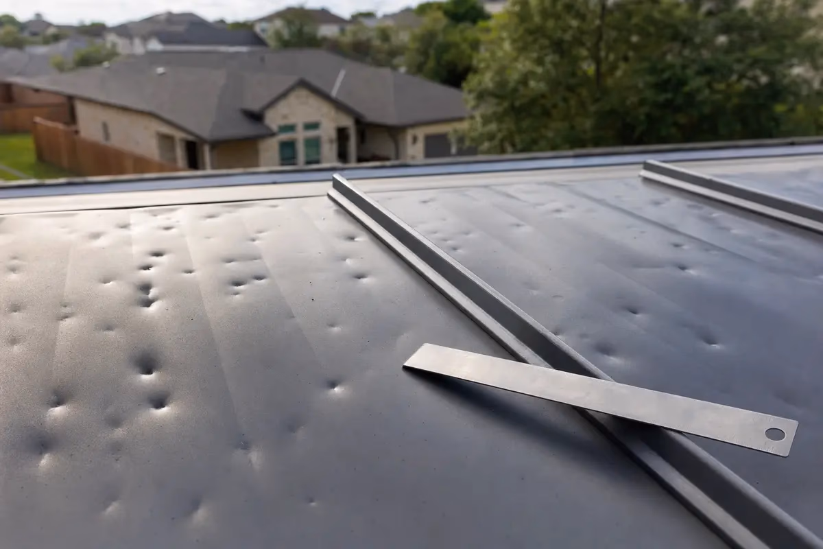 Close-up inspection of hail dents on a standing seam metal roof panel with tape measure for scale