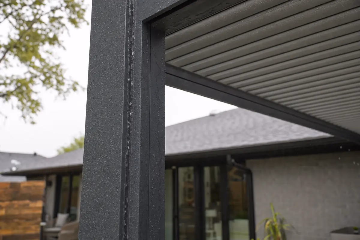 Closed aluminum louvered pergola shedding rain through hidden drainage channels in posts
