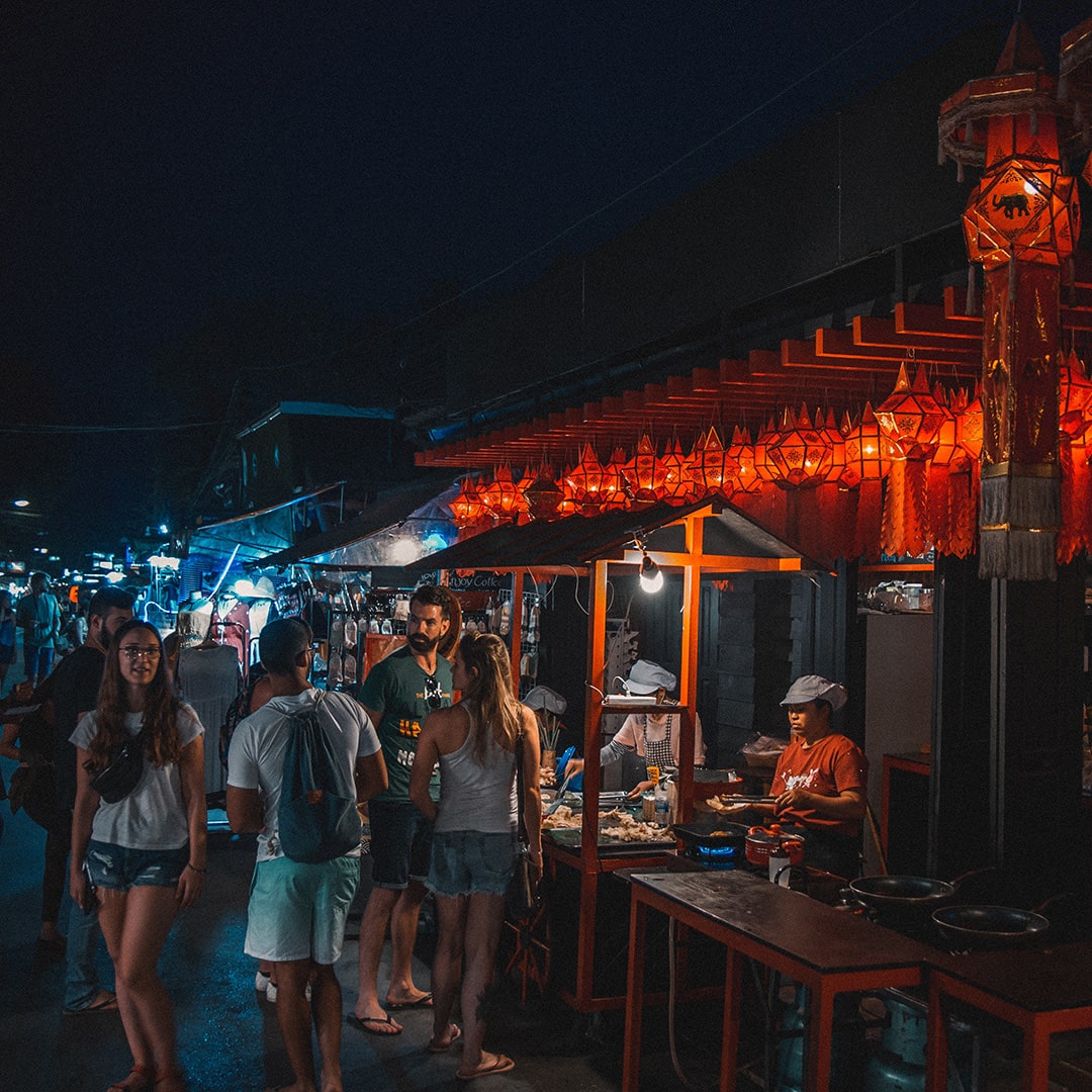 a thai street food establishment at night with customers ordering food
