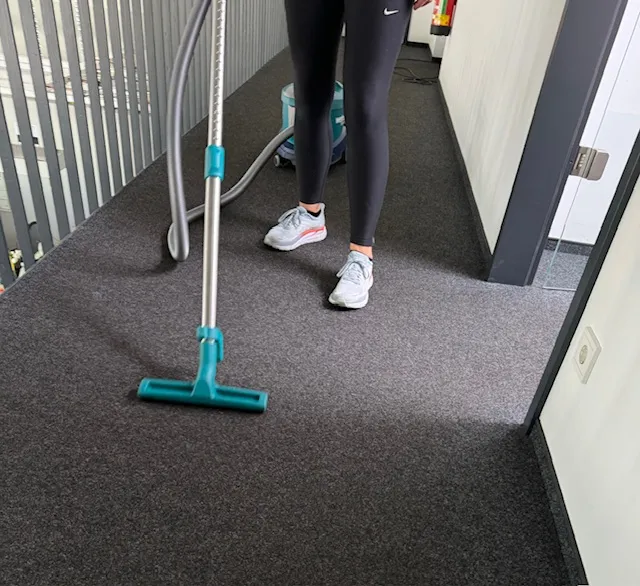 Mitarbeiterin saugt den den Teppichboden in einem Büro. Professionelle Büroreinigung als Unterhaltsreinigung.
