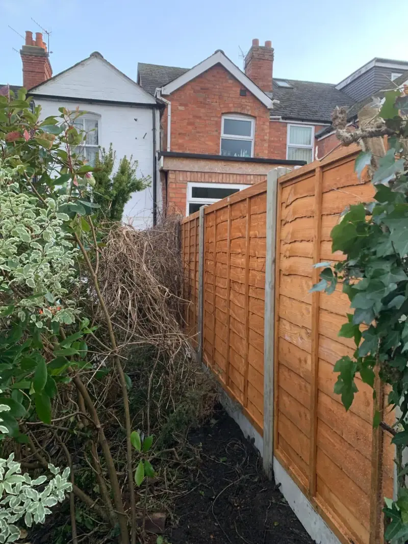 strong fence with concrete posts behind hedge