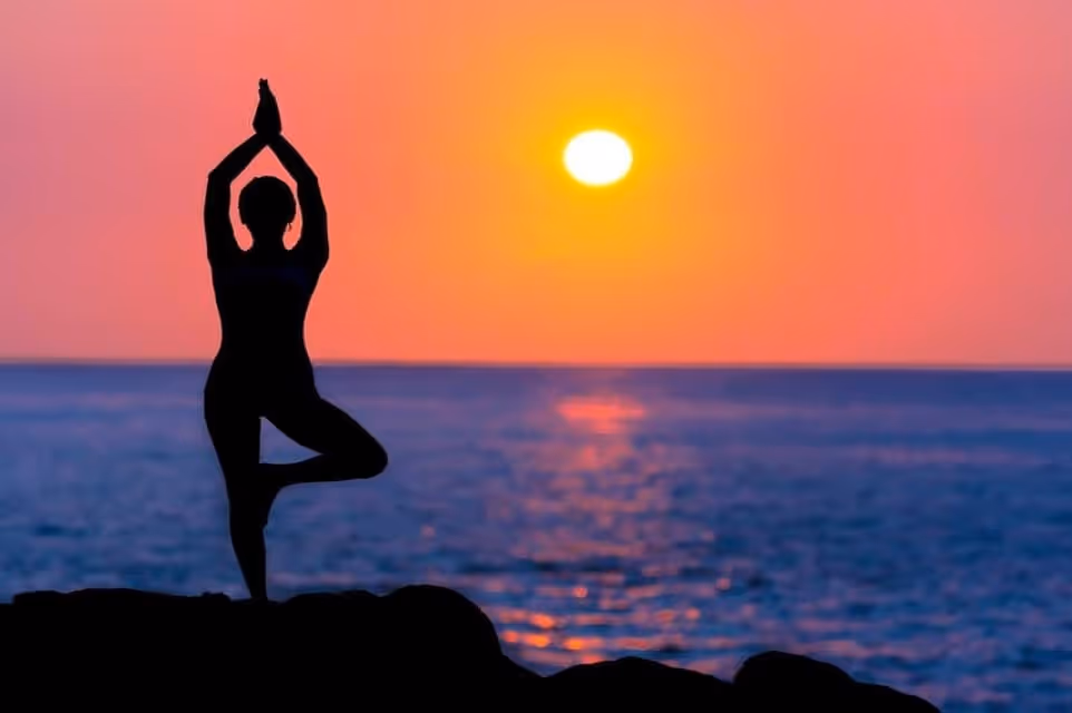 Woman doing yoga by the sea at sunset