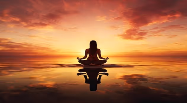 A woman sitting in front of a sunset, chanting mantras and meditating.