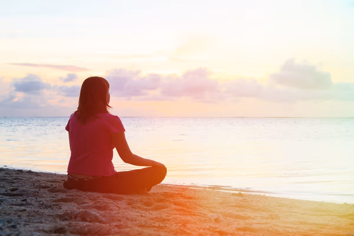 A woman meditating and doing breathing exercises on the beach.