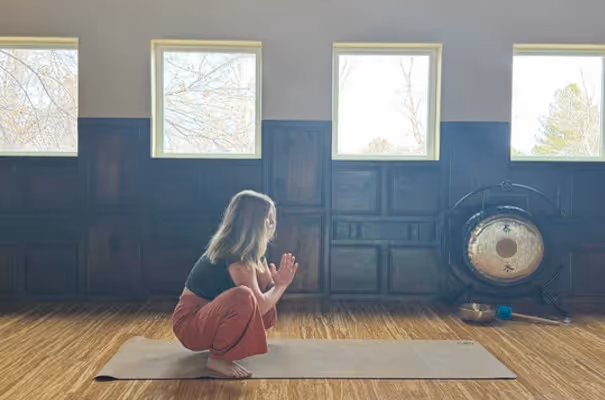 A yogi woman sits in a room with light shining through the window and a Chinese cymbal.