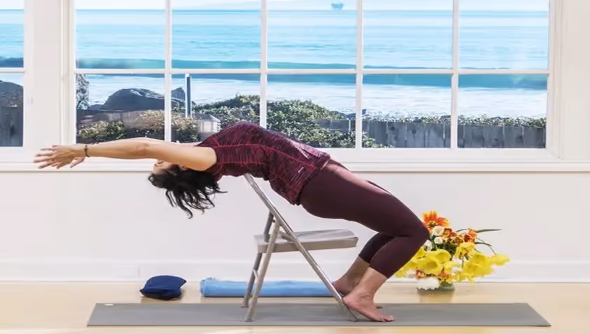 Yogi woman practicing yoga using a chair in front of a beautiful view of the sea