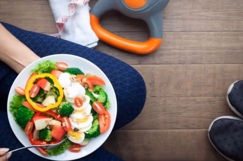 Salad plate in the hands of an athletic woman with shoes and dumbbells