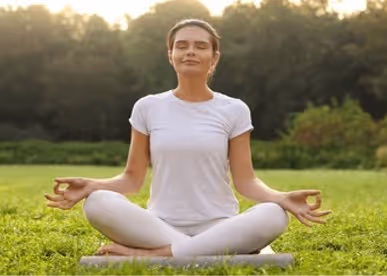 A woman in a white dress sits in Padmasana Lotus Pose in nature.