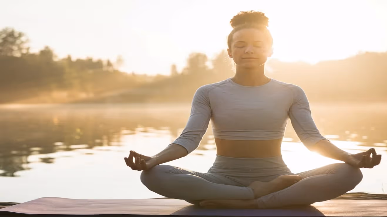 Yogi lady with her back to the lake at sunrise in lotus position
