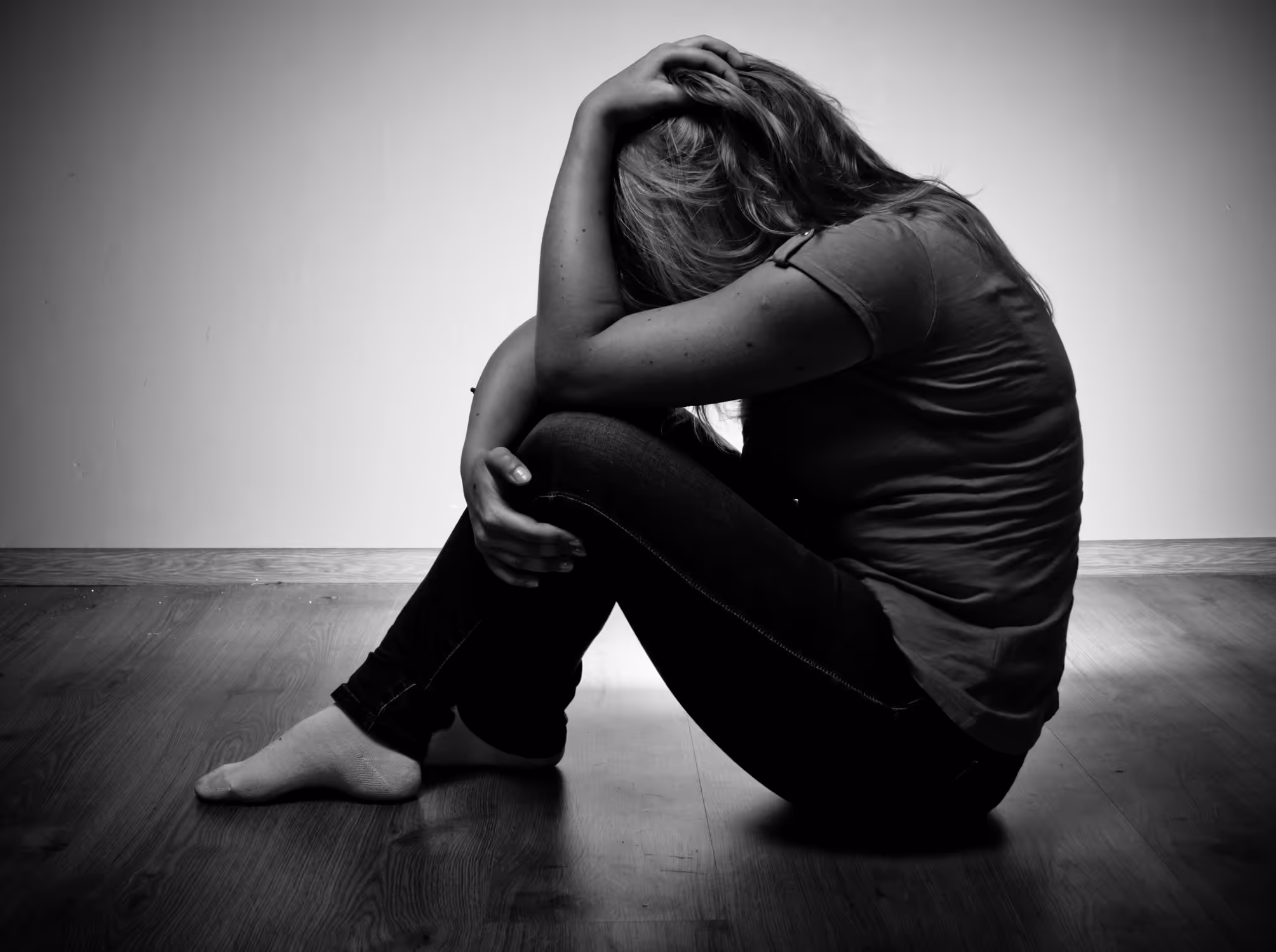 Black and white photo of a woman hugging her knees and placing her hands on her head in grief
