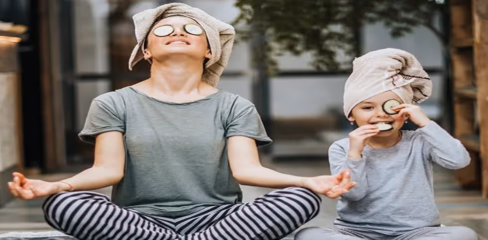 Child and teenage girl in lotus position with towel on head and cucumber slices on eyes happy