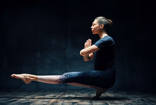 Yogi lady sitting on tiptoes, one leg extended and the other leg extended in front, wearing a black dress