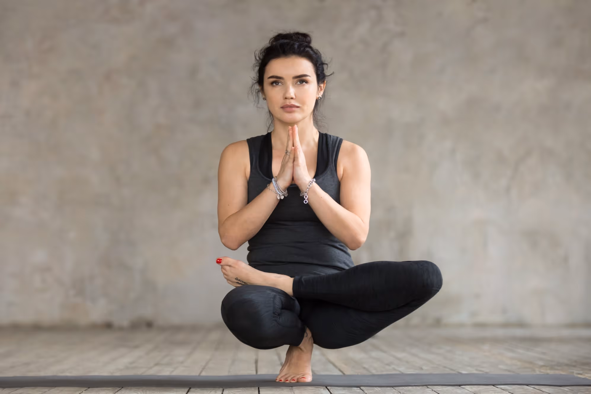 Yogi lady in black dress on mat doing Half Lotus Toe Balance Pose 