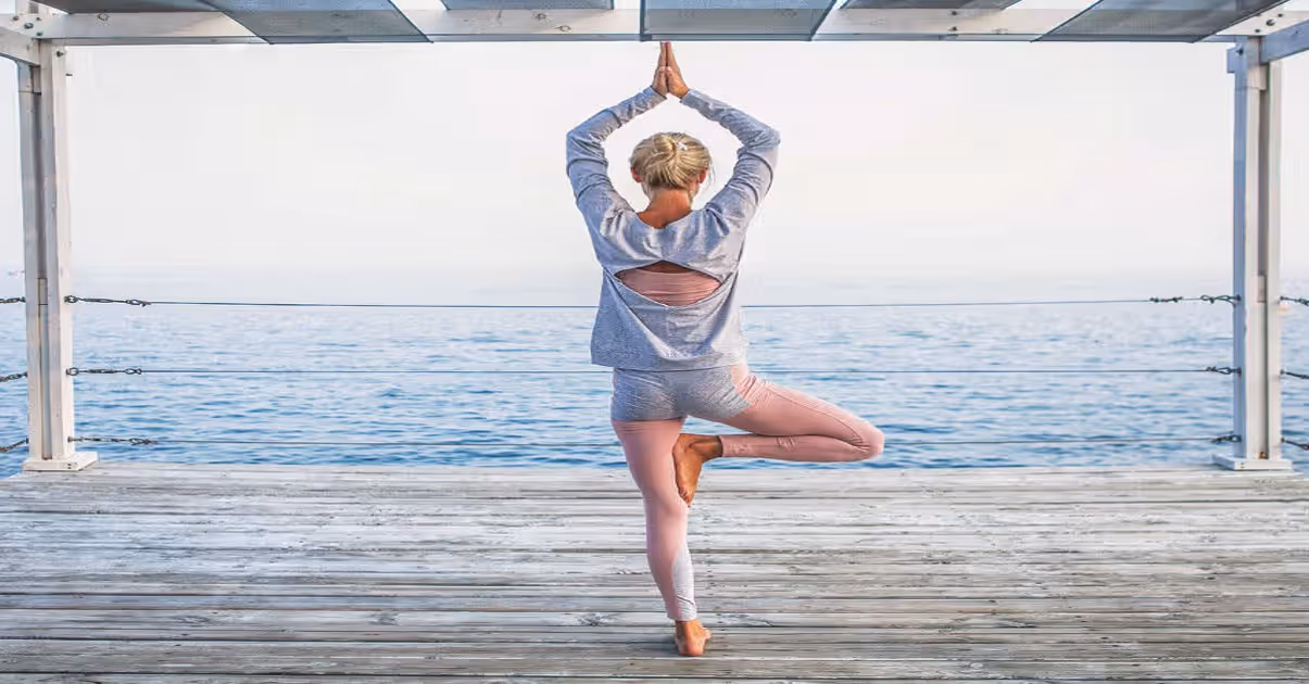 Yogi lady standing on one leg facing the sea on the pier