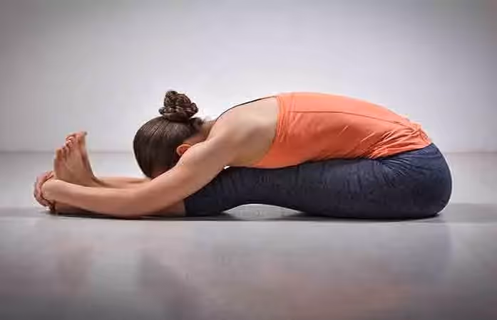 The yogi woman sits on the mat with her legs extended, bent at the waist and holding the soles of her feet with her hands.