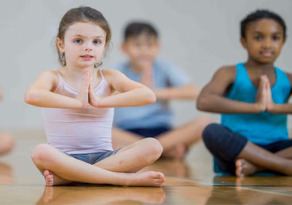 Three yogi children sitting in lotus position with hands clasped