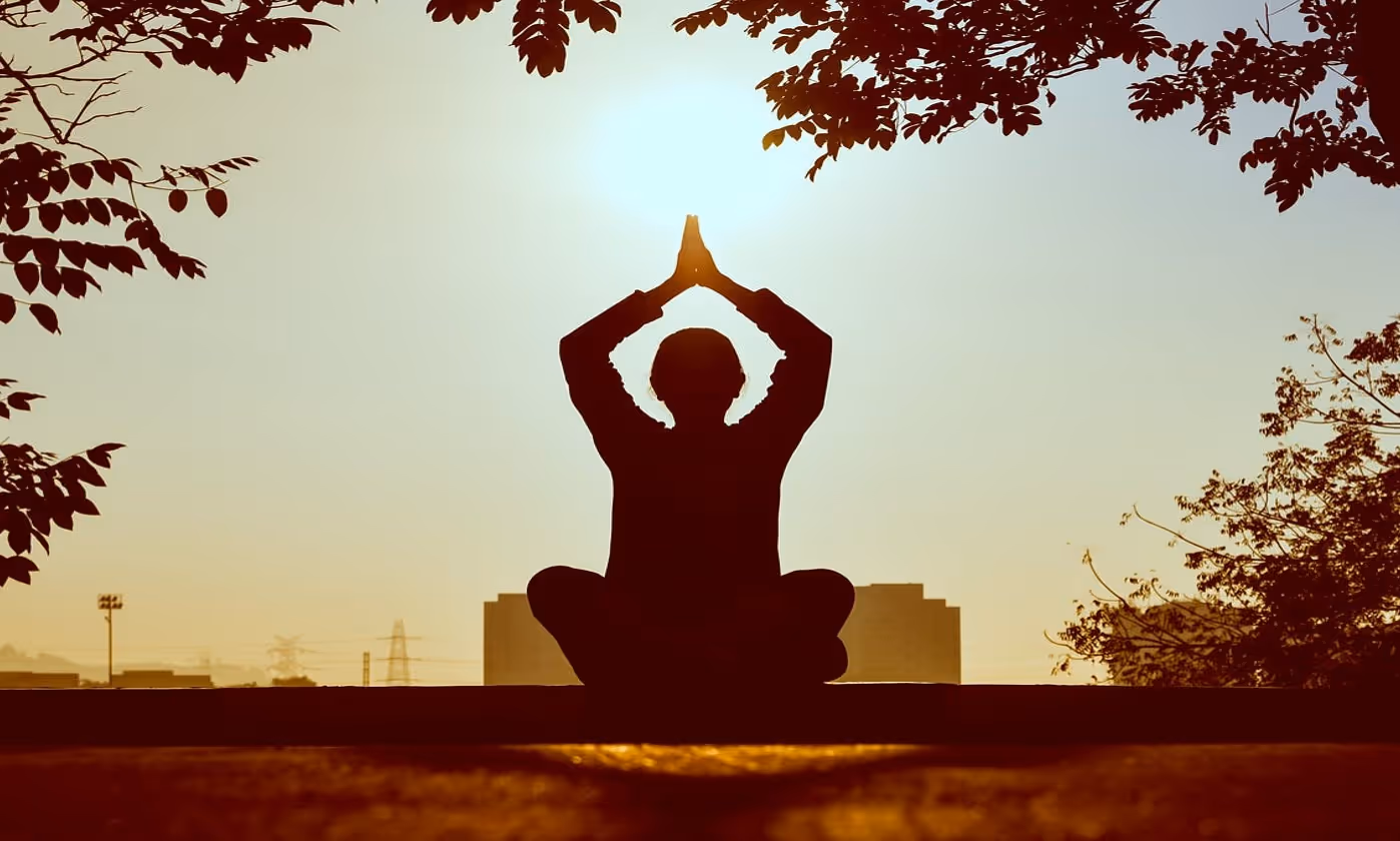 A man sitting in lotus position in front of city buildings next to trees.