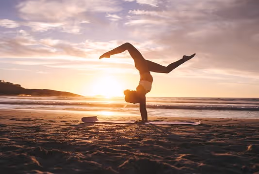 Yogi lady standing on her hands by the beach and sunset